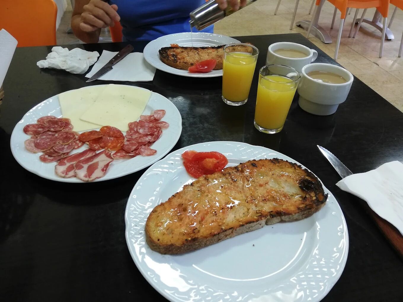 A breakfast table with plates of food, including sliced meats, cheese, and a grilled item, along with glasses of orange juice and coffee.