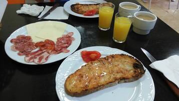 A breakfast table with plates of food, including sliced meats, cheese, and a grilled item, along with glasses of orange juice and coffee.