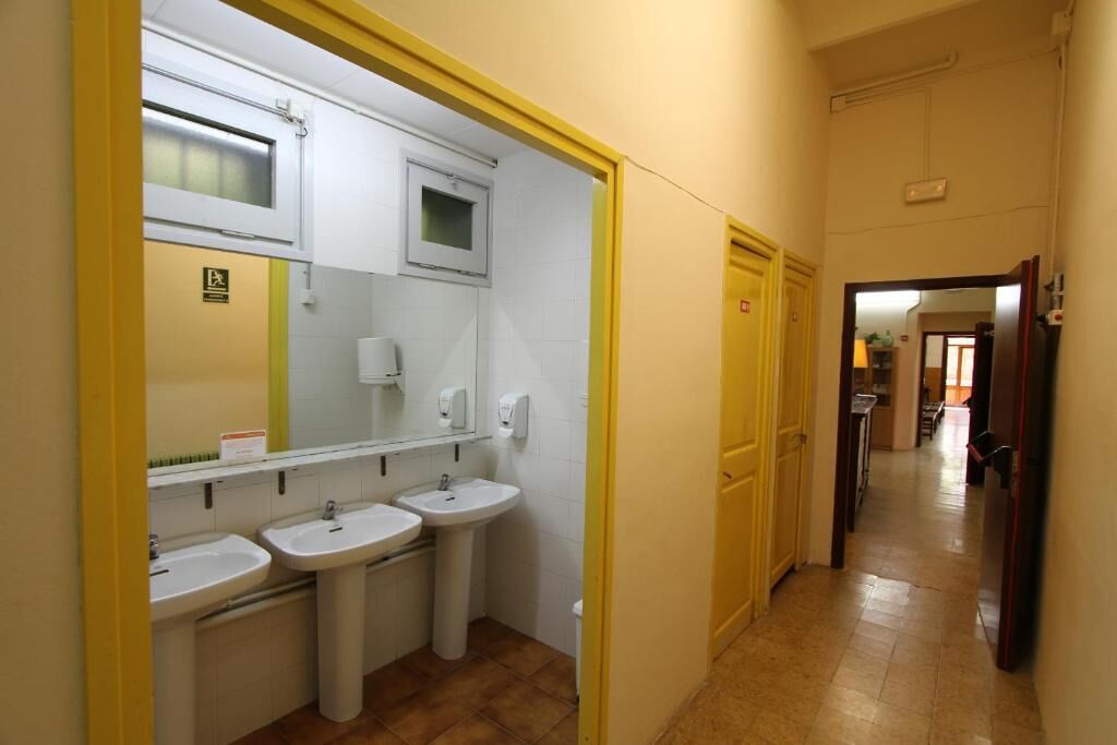 A hallway leading to a bathroom with three sinks and a mirror.