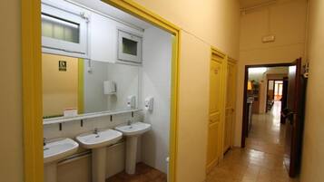 A hallway leading to a bathroom with three sinks and a mirror.
