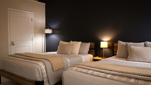 Habitación de hotel con dos camas, una puerta, una lámpara de pared y una mesita de noche.