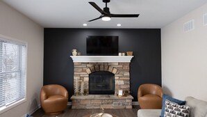 Una sala de estar con chimenea de piedra, sillones de cuero, ventilador de techo y un televisor de pantalla plana grande.