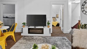 Una sala de estar moderna con una televisión de pantalla plana, sillas amarillas, un mueble blanco para entretenimiento y una alfombra gris.
