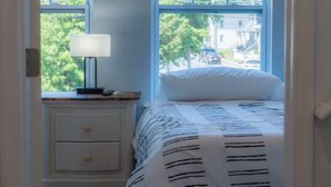 Un dormitorio con cama, mesita de noche, lámpara y ventana con vista a la calle.