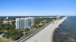 Paesaggio costiero con un hotel fronte spiaggia che si sviluppa su più piani, una strada parallela alla spiaggia e cielo sereno.