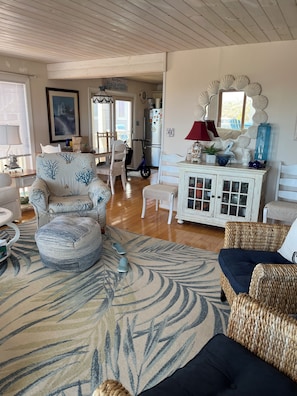 A cozy living room with a wooden ceiling, a dining area with chairs, a refrigerator, and a decorative mirror.