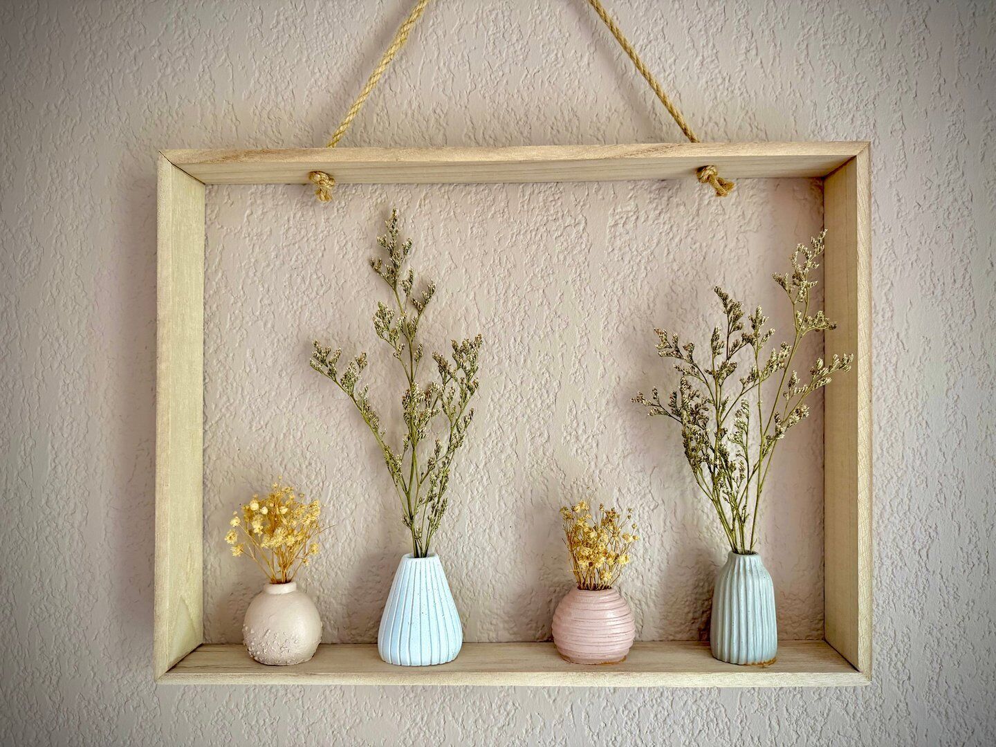 A wooden shelf with four vases containing dried flowers against a textured wall.