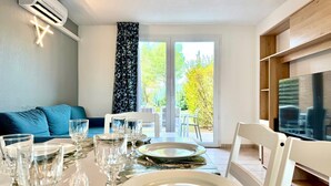 Zona pranzo con tavolo apparecchiato per sei persone, un divano e una televisione sullo sfondo.