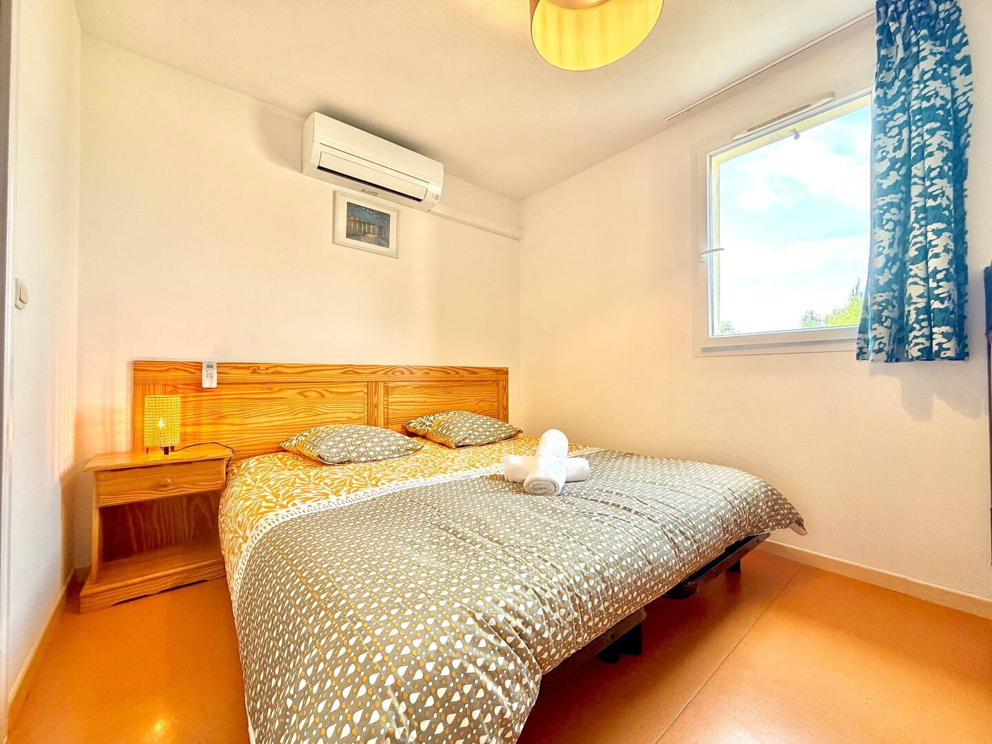 Una camera da letto con una testiera in legno, un letto con lenzuola a fantasia, un comodino con una lampada e una finestra con tende blu.
