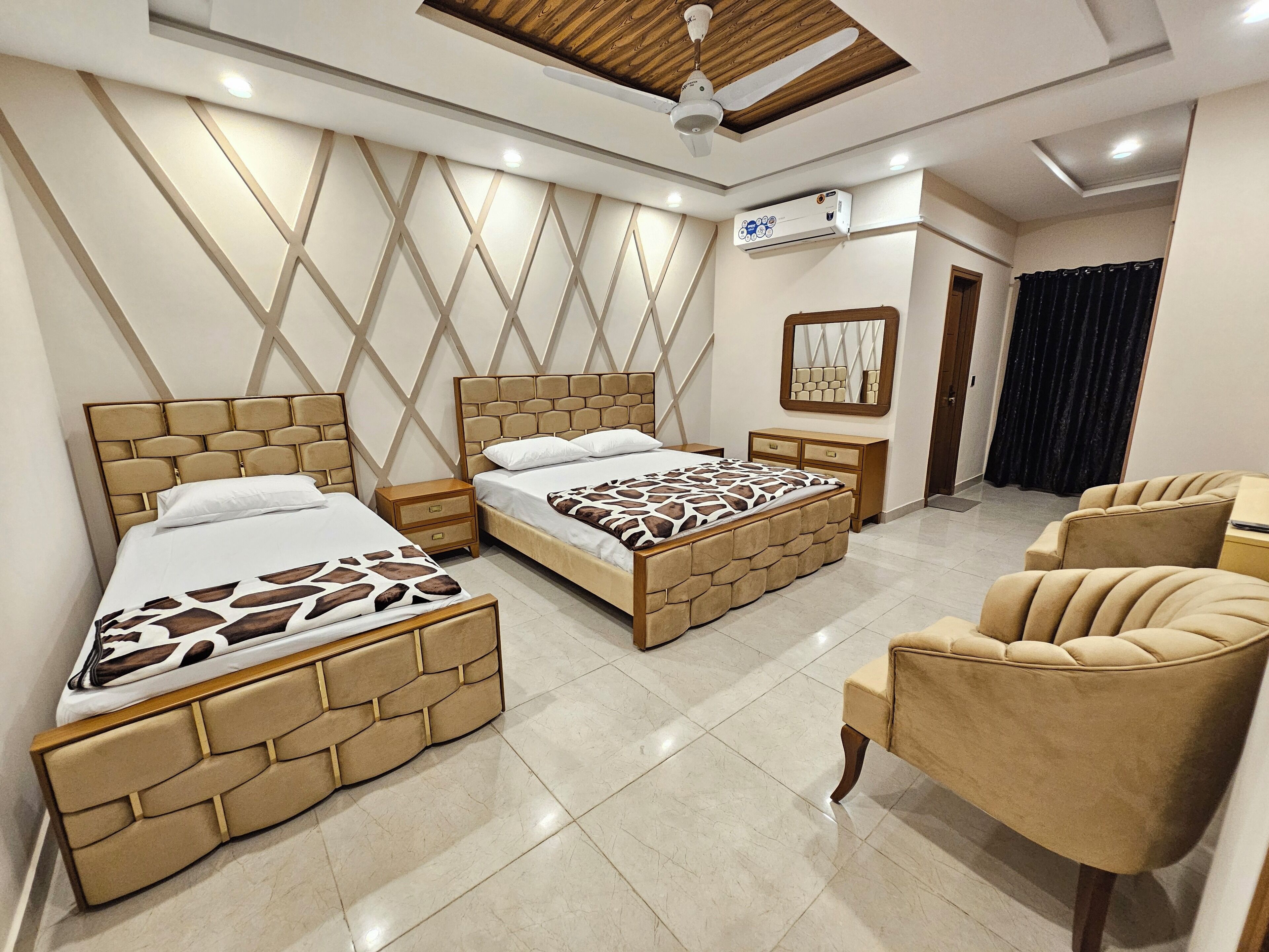 A hotel room with two beds, a ceiling fan, a mirror, a small table, and a chair.