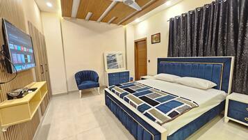 A modern bedroom with a large bed, a TV mounted on the wall, a chair, and a wooden ceiling.