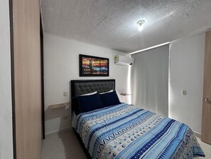 Une chambre à coucher comprenant un lit, une table de chevet, un climatiseur fixé au mur et un tableau encadré accroché au mur.