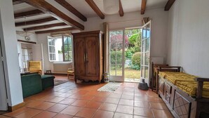 A spacious room with a tiled floor, a wooden cabinet, a green sofa, and a bed with a yellow blanket. - 2-star house - Jardin Clos - Beach, forest and shops on foot (Saint-Hilaire-de-Riez)