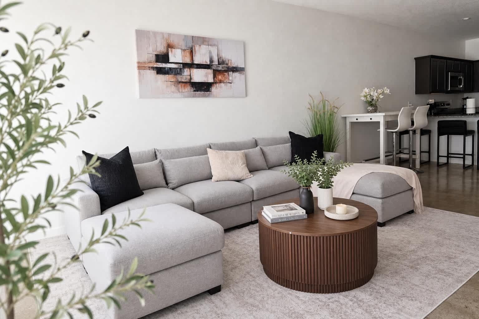 A modern living room with a grey sectional sofa, a round wooden coffee table, and a minimalist abstract painting on the wall.
