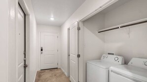 Ett tvättrum med tvättmaskin och torktumlare, en vit dörr och en beige matta.