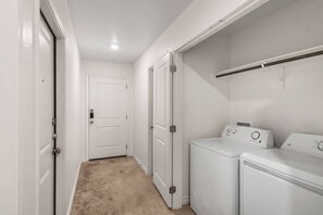 A laundry room with a washing machine and dryer, a white door, and a beige carpet.