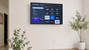 En platt-TV som är monterad på en vägg och visar ett Roku-gränssnitt med olika streamingtjänster, samt ett erbjudande om 50 % rabatt på ett abonnemang.