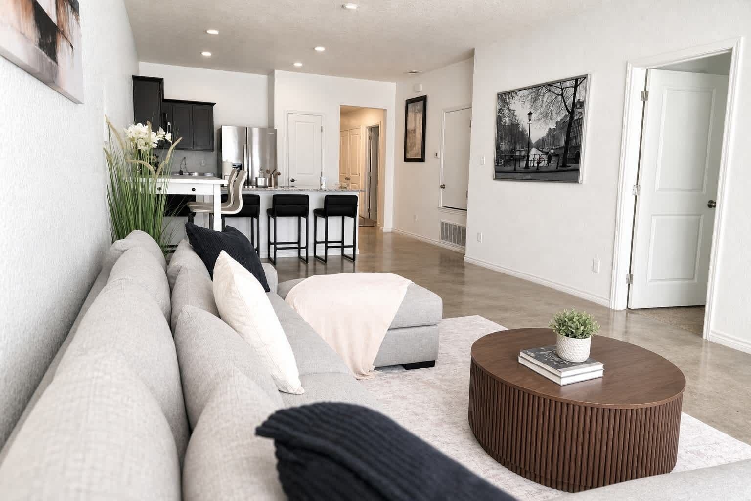 A modern living room with a sofa, ottoman, coffee table, and a kitchen in the background.
