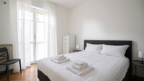Ein Hotelzimmer mit einem großen Bett, einem Schreibtisch, einem Stuhl, einem Kleiderschrank und einem Fenster mit durchsichtigen Vorhängen.