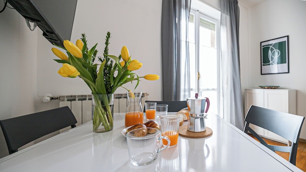 Ein Frühstückstisch mit einer Vase voller gelber Tulpen, einer Kaffeemaschine und Orangensaft.