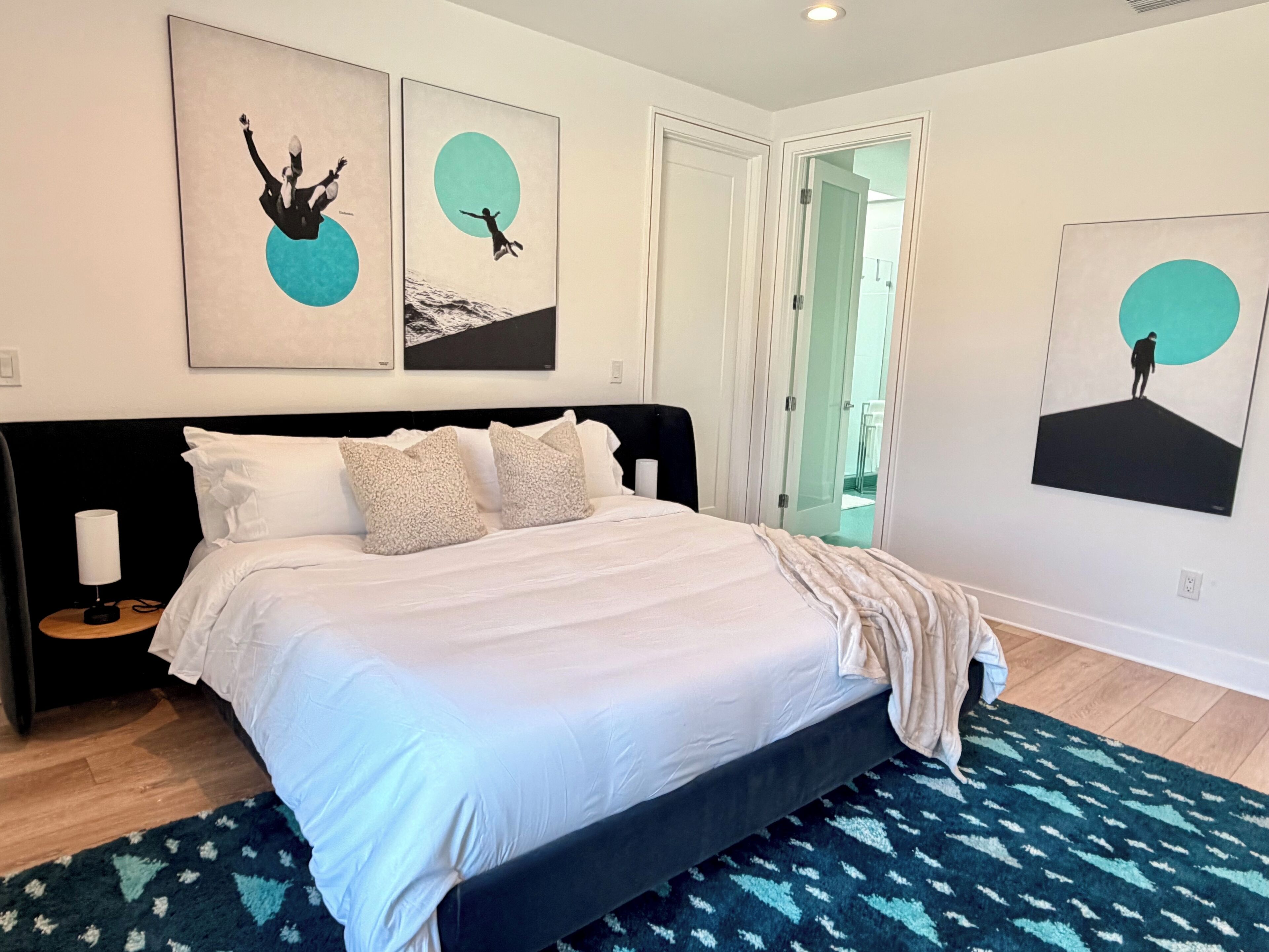 A modern bedroom with a large bed, a nightstand, and a wall with three framed artworks.