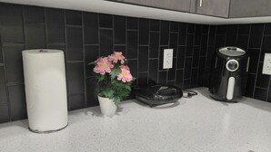 A kitchen with dark tiled backsplash, a white countertop, a roll of paper towels, a potted plant with pink flowers, and a coffee maker. - Unwind in this serene environment with close proximity to the airport. (Calgary)