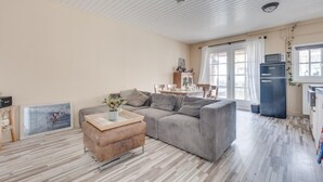 Een woonkamer met een grijze bank, een houten salontafel, en een keukenhoek met een zwarte koelkast.