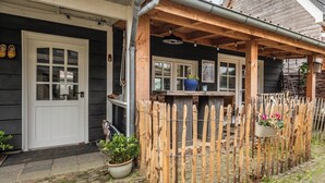 Een houten huis met een veranda, een witte deur en een kleine tuin met planten in potten.