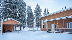 A wooden cabin with a covered porch and a separate garage, surrounded by snow-covered trees. - Villa Siltasaari (Sotkamo)