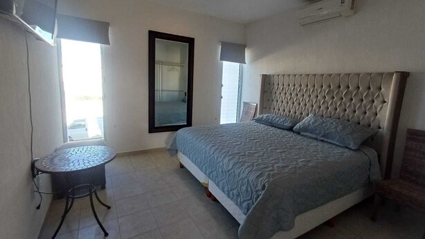 Een slaapkamer met een bed, een klein rond tafeltje, een spiegel en een airconditioner.