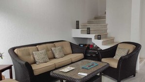 Een woonkamer met een bank, twee fauteuils, een salontafel en een trap.