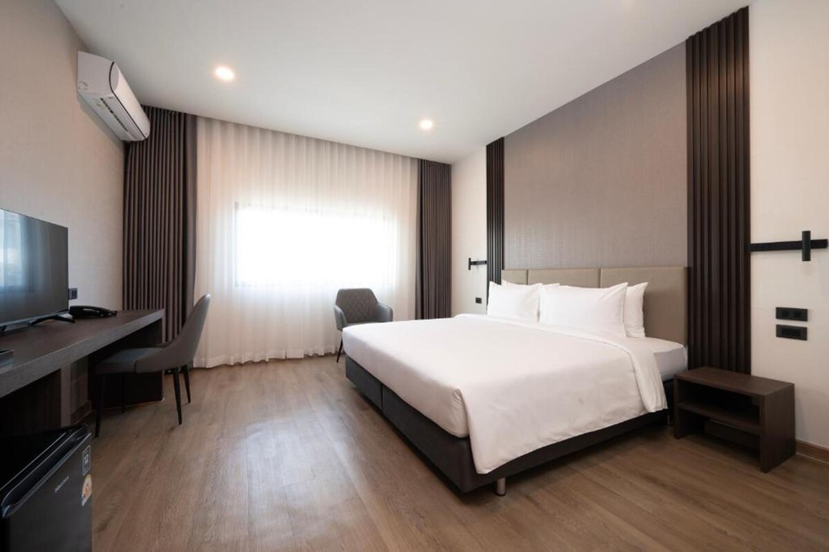 A hotel room with a bed, a desk with a chair, a television, and an air conditioning unit.
