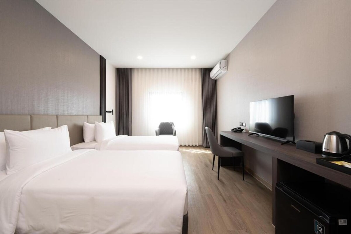 A hotel room with two beds, a desk with a television, a chair, and a coffee maker.