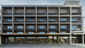 Ein mehrstöckiges Hotel mit modernem Design, mit Balkonen auf jeder Etage und einem Restaurant/Lounge-Bereich im Erdgeschoss.