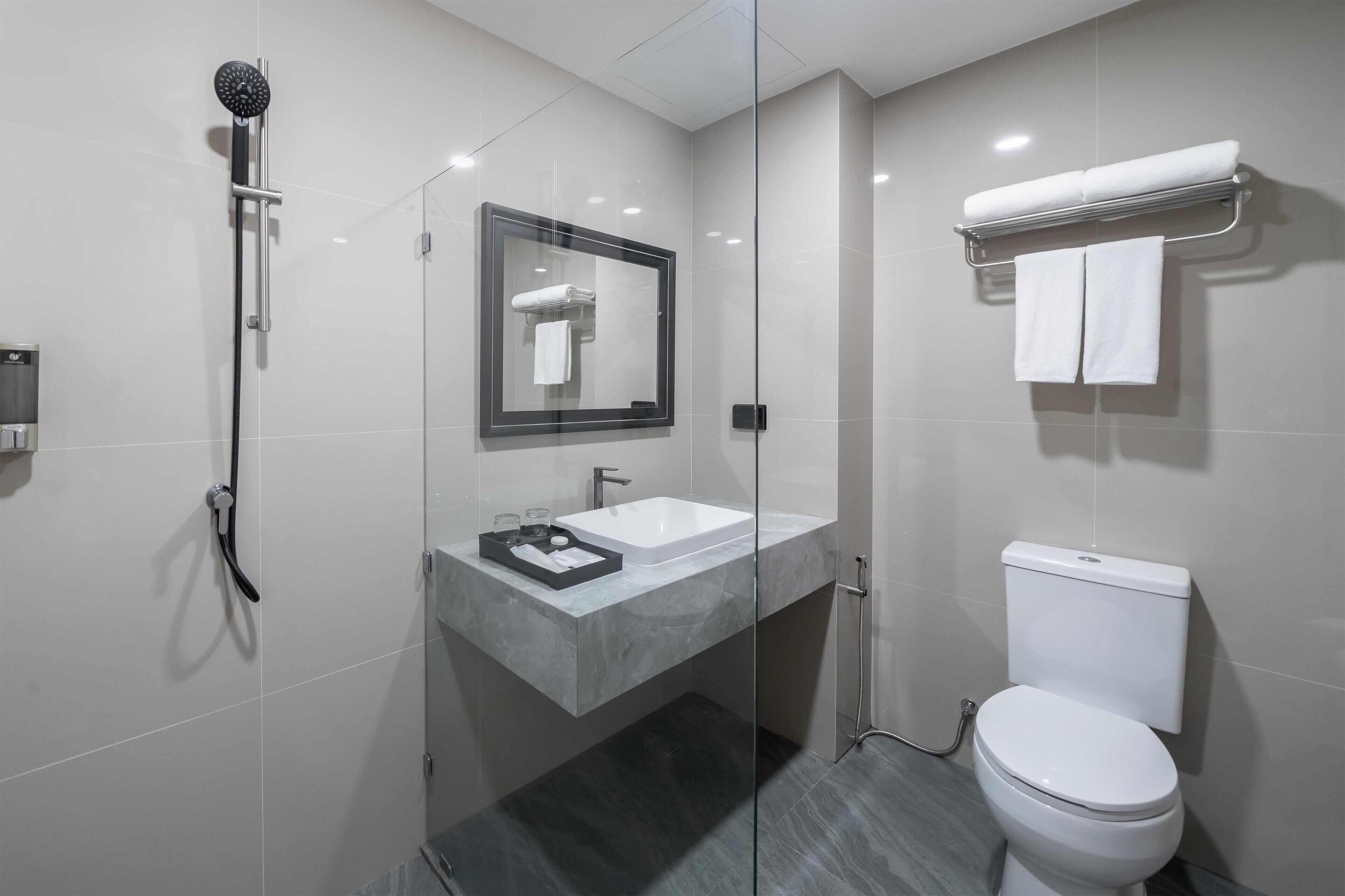 Un baño moderno con ducha envuelta en vidrio, lavamanos blanco y retrete.