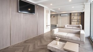 Ein modernes Wohnzimmer mit einem großen Flachbildfernseher an der Wand, einem beigen Sofa und einem Parkettboden mit Zickzackmuster.