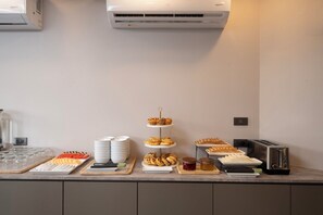 A buffet counter with various food items, a toaster, and a wall-mounted air conditioner. - Surestay Plus By Bw Ramkhamhaeng Airport Rail Link Bangkok (Bangkok)