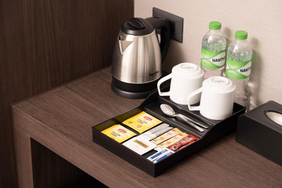 A neatly arranged hotel room with a coffee maker, two cups, two bottles of water, a tray with coffee packets, and a spoon.
