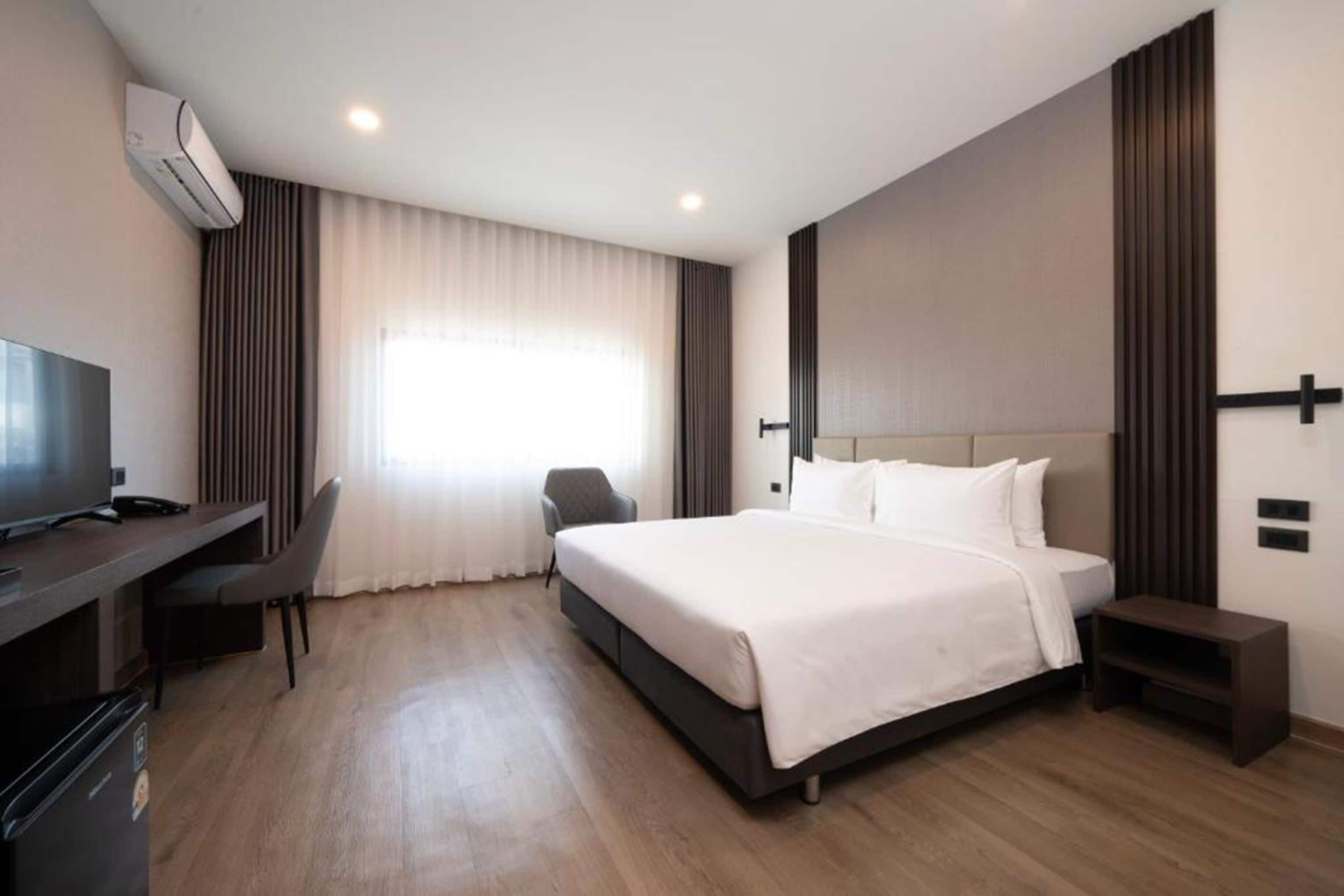 A hotel room with a bed, a desk with a chair, a television, and an air conditioning unit.