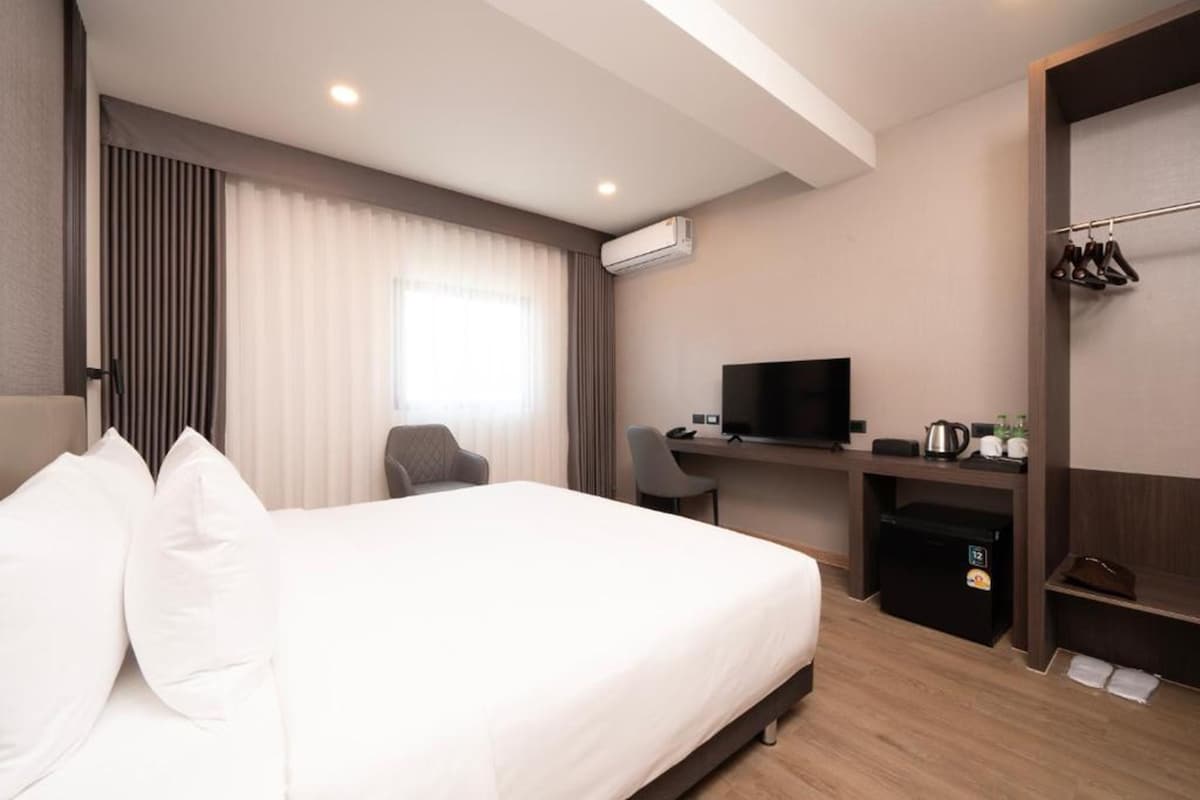A hotel room with a bed, a desk, a television, a wardrobe, and an air conditioning unit.