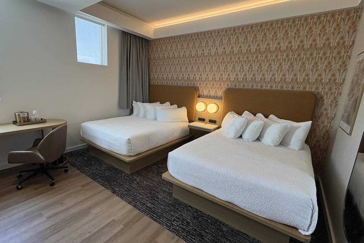Une chambre d’hôtel avec deux lits, un bureau, une chaise et une fenêtre.