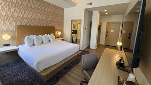 A hotel room with a large bed, a desk with a computer, a chair, and a mirror.