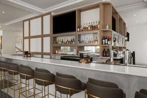 A bar area with a long counter, multiple shelves of bottles, and bar stools. - Aiden By Best Western Kansas City Downtown (Kansas City)