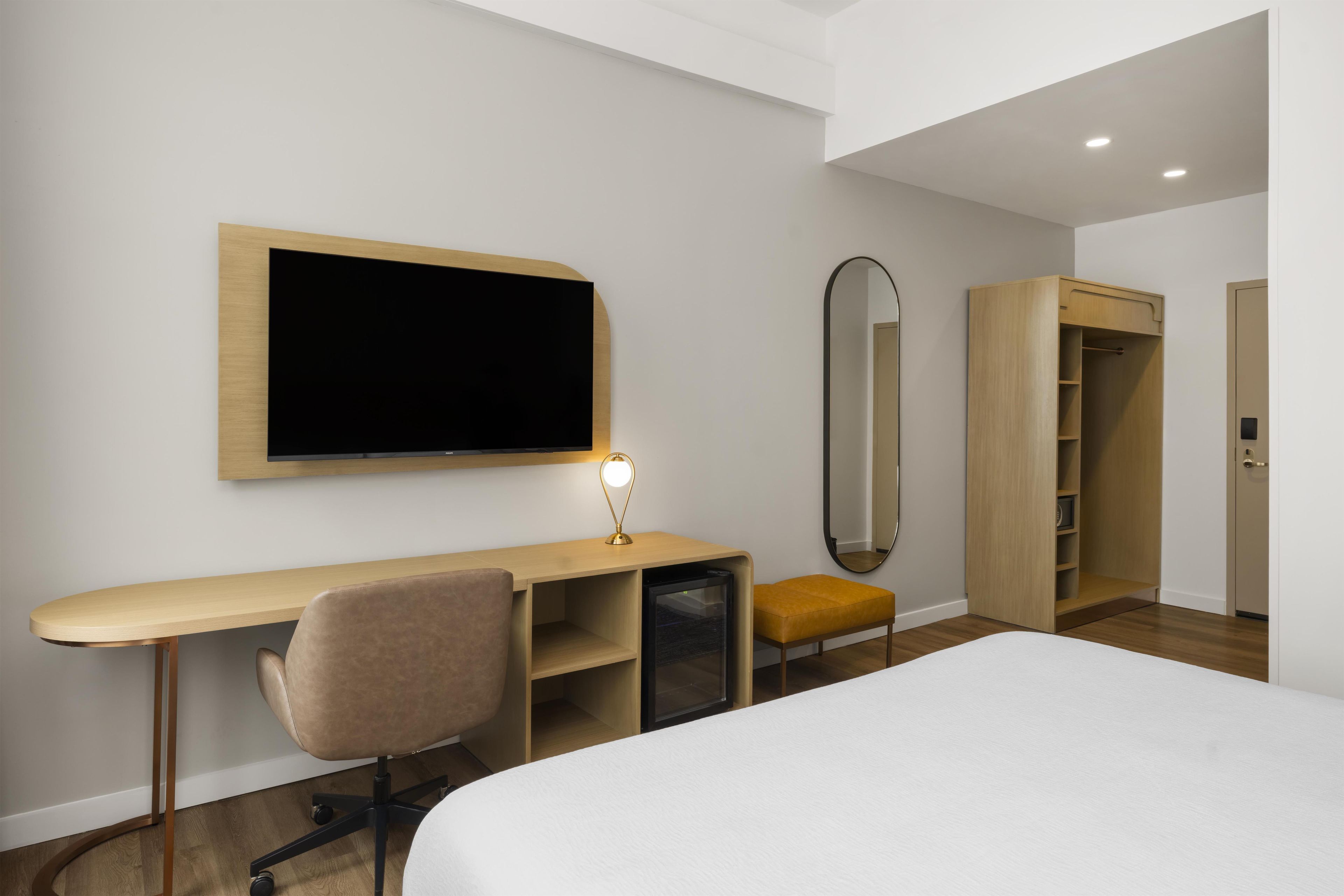 Une chambre d’hôtel comprenant un lit, un bureau avec une chaise, une télévision, un miroir et une armoire.