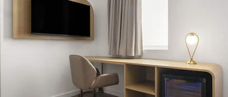 A modern room with a flat-screen TV mounted on the wall, a desk with a computer, a chair, and a lamp.