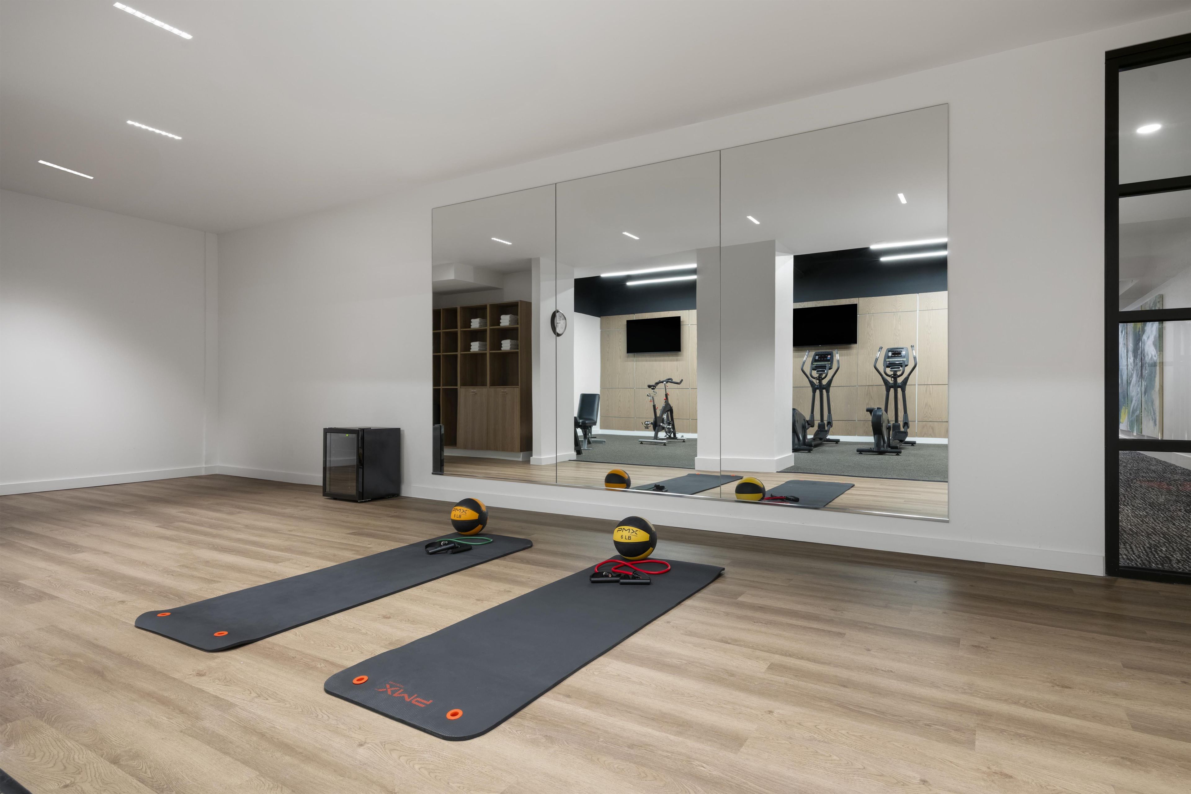 Ginásio com colchonetes de exercício, espelho e equipamentos de fitness.
