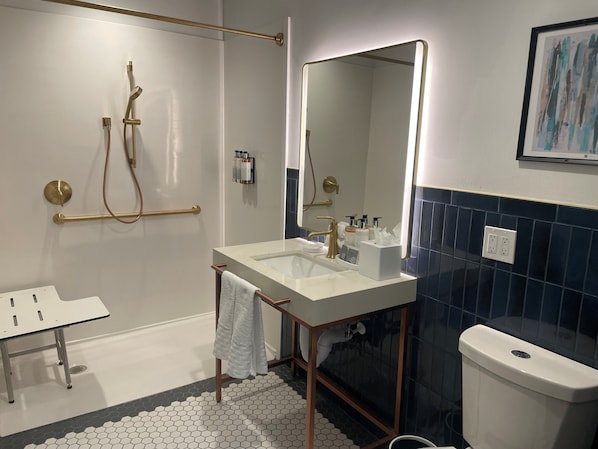A bathroom with a glass-enclosed shower, a white sink with a gold faucet, a large mirror, and a toilet. - Aiden By Best Western Kansas City Downtown (Kansas City)
