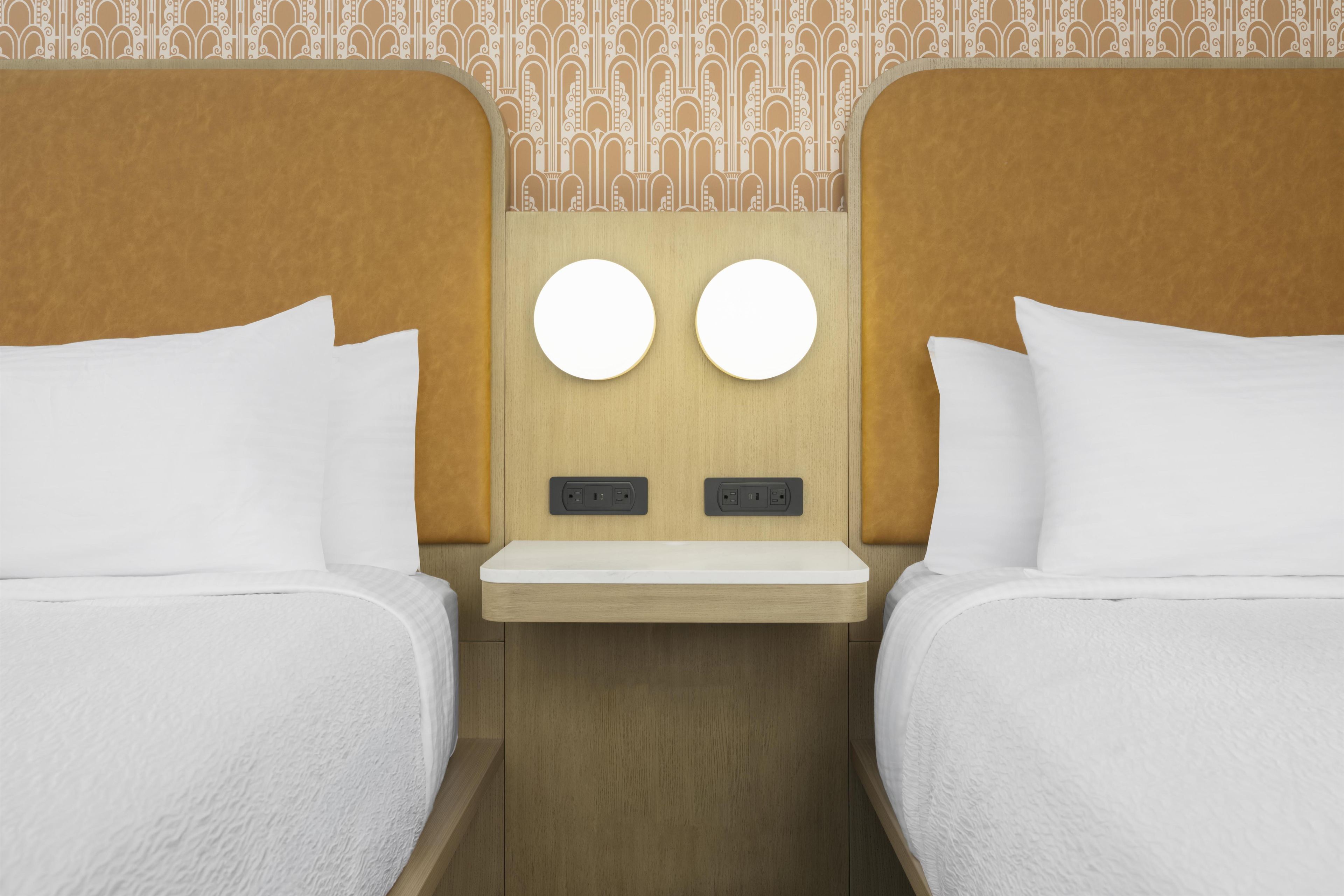Habitación de hotel con dos camas, una mesita de noche y una lámpara fijada a la pared.