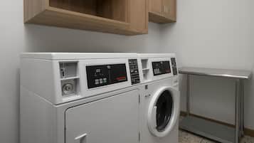 A front-loading white washer and dryer unit with a digital control panel, a wooden cabinet above, and a metal shelf to the right.
