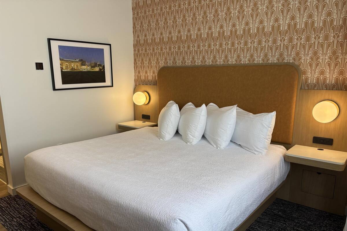 Un lit bien fait, avec des draps blancs, une tête de lit et deux lampes de chevet.